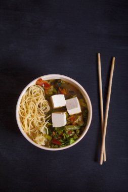 Sebzeli Japon çorbası, makarna, tofu peyniri, siyah arka planda çubuklar. Düz yatıyordu. Kürekleri kopyala