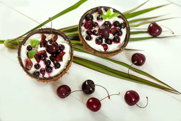 配上奶油 樱桃和椰子杯中的醋栗 以及棕榈叶和白色木制餐桌的甜点 — 图库照片