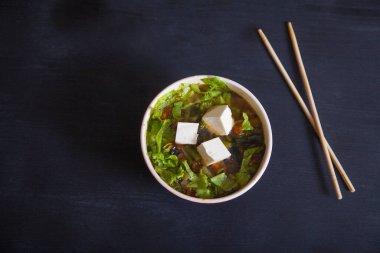Tofu peynirli Japon çorbası, yeşil fasulye, sebze, şifalı otlar, siyah arka planda bambu çubukları. Kürekleri kopyala