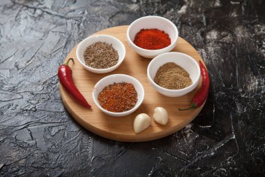 Yerdeki baharatlar kimyon, beyaz porselen bardaklardaki biber, sarımsak ve acı biber siyah arka plandaki ahşap tezgahta duruyor.