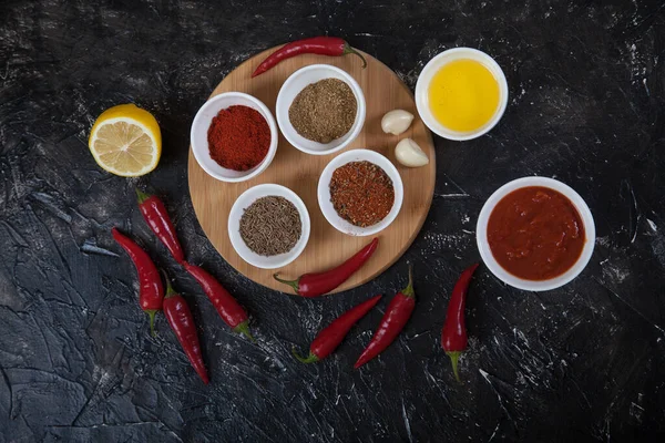 Harissa, baharat kimyonları, beyaz porselen bardaklarda biberler, sarımsak ve acı biber biberleri ve ahşap bir tezgahta siyah arka planda sebze yağı standı. yatay olarak.