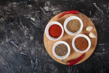 Baharatlı kimyon, beyaz porselen bardaklarda biber, sarımsak ve acı biber, siyah arka planda ahşap bir standın üzerinde duruyor. Kürekleri kopyala.