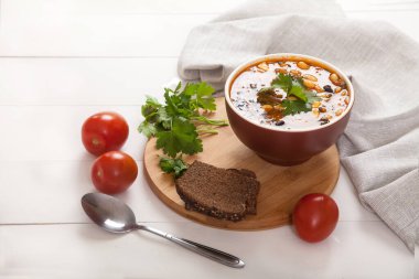 Toprak kabında vejetaryen fasulyesi ve zeytin çorbası, çavdar ekmeği, kaşık ve keten peçete beyaz ahşap bir masa üzerinde.