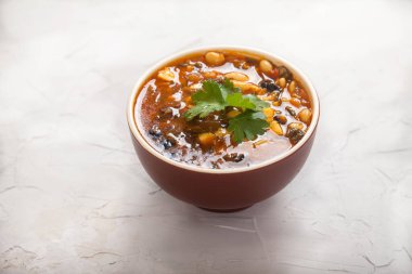 Domatesli, zeytinli ve maydanozlu toprak kabında fasulye çorbası. Beyaz beton arka planda. Düz yatıyordu