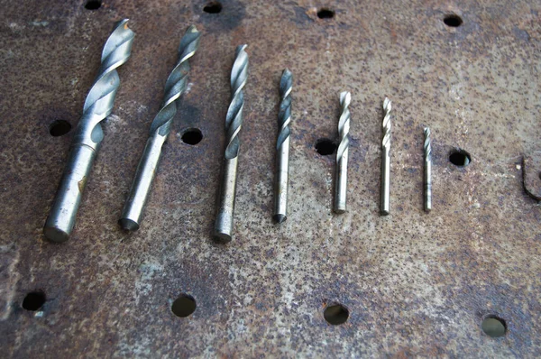 Drills of different diameters lie on a rusty sheet of metal — Stock Photo, Image