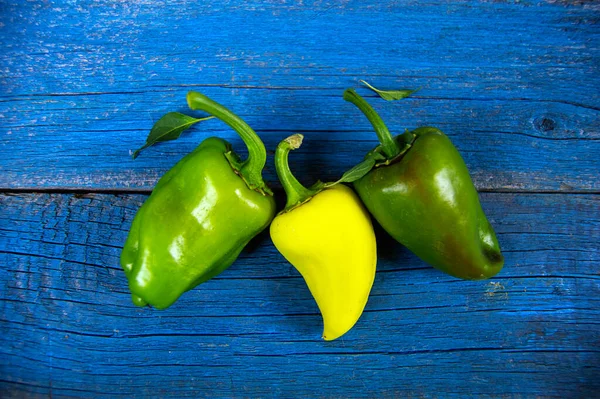 Sarı ve yeşil dolmalık biberler kırsal ahşap arka planda yatar.