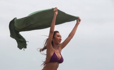 Tatlı seksi Bayan mor bikini ile yeşil kumaş havaya kaldır ve sallayarak, gülümseme ve mutlu yüz ile,