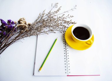 Sarı seramik kahve fincanı ve ilgili açılan kitap, Kuru çiçek, yanında beyaz masa koymak kalem