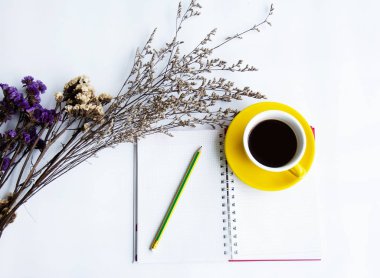 Sarı seramik kahve fincanı ve ilgili açılan kitap, Kuru çiçek, yanında beyaz masa koymak kalem