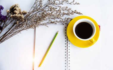 Sarı seramik kahve fincanı ve kalem beyaz tablo, Kuru çiçek, yanında açık kitap etrafında bulanık ışık koymak.