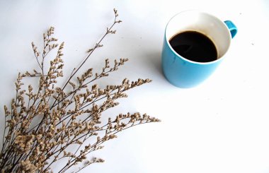 Siyah kahve yanında beyaz zemin üzerine kuru çiçek koymak ile kahve fincanı