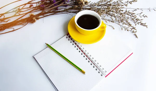 黄色のセラミック コーヒー カップと白いテーブルの上は ドライフラワー 横の開いた本に鉛筆 — ストック写真