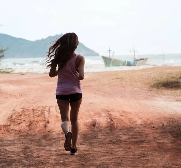 The back side of lady in exercise suit is jogging on the beach,in the morning,for exercise,built fit and firm body and good health.blurry light design background.