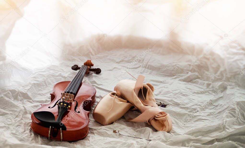 The wooden violin put beside ballet shoes,on background,warm light tone,blurry light design background