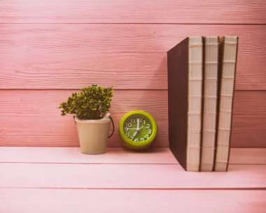 Kitaplar yığılmış soyut artdesign arka plan, yeşil çalar saat ve seramik kil pot bitki ahşap ahşap tahta koymak