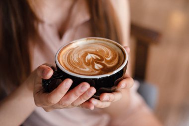 Bayan ellerde kapuçino fincan seçici odak, bulanık ışık tasarım arka plan