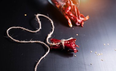 Kenevir halat ile bağlı kurutulmuş biber seçici odak, siyah tahta koymak, bulanık ışık tasarım arka plan