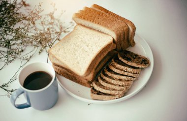 Dilimlenmiş ekmeğin bulanık ışık tasarım arka planı, beyaz masa, vintage ve sanat tonu üzerine, siyah kahve ile mavi seramik kahve fincanı yanına koymak