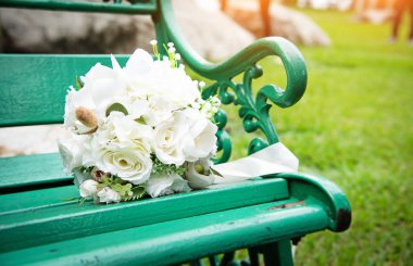 Yeşil sandalyeye konulan gül buketinin seçici odağında, bir parkta, bulanık ışık