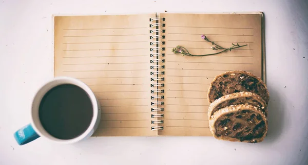 本とミックスフルーツパン ホワイトデスク ヴィンテージ アートトーンの横に置かれたブラックコーヒーとブルーセラミックコーヒーカップのぼやけた明るいデザインの背景 — ストック写真