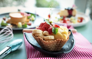 Muz, çilek ve nane yaprağı ile meyvedondurma waffle sepeti koymak, porsiyon için hazırlamak, çevresinde bulanık ışık