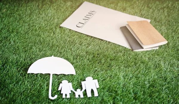 The family paper cut put under the umbrella paper cut,on green grass ground floor,sigh and symbol of safety life under protection,blurry light around