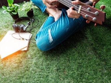Humand el ukulele oynuyor, yeşil çim zemin katta oturan, etrafında bulanık ışık