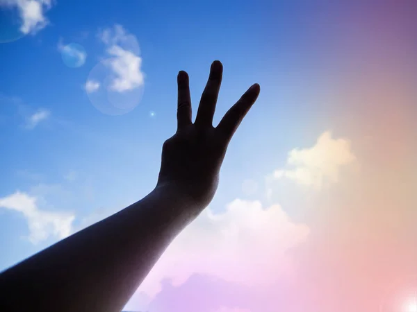 The silhouette hand show three fingers up in the air,Hand sign reach to the sky background,lens flare effect,blurry light around
