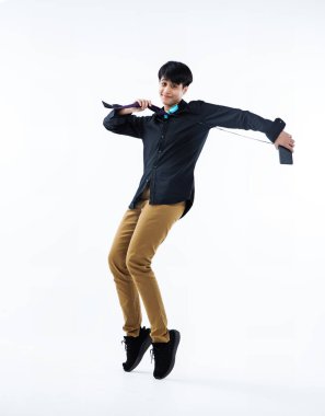 Genç öğrenci cep telefonunu elinde tutuyor ve kulak başıyla boynunu örtüyor ve zıplıyor, mutlu duygular, genç yaşam tarzı, beyaz arka planda.