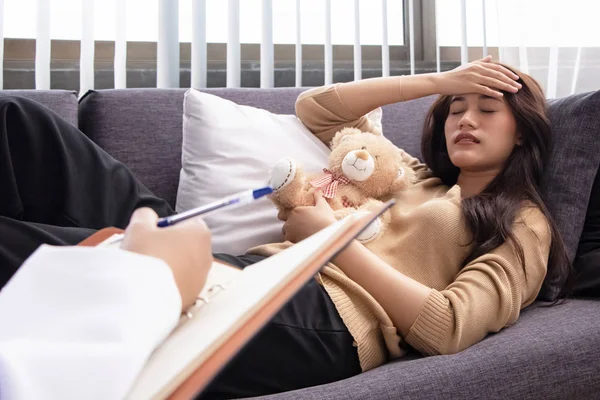 The stressed woman laying down on sofa,hold little doll on hand,the patient was encourage by doctor hand,mental illness,negative emotion,depressive disorder syndrome