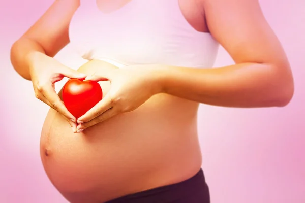 小さな赤い心の選択的な焦点で妊娠中の女性の手 署名と愛とケアのシンボルによって保持されていた — ストック写真