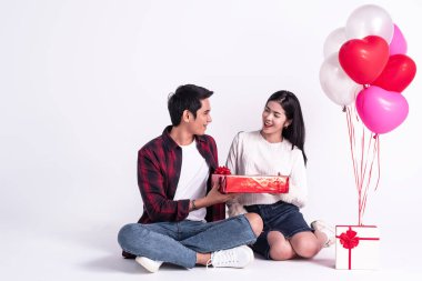 Güzel kadın kırmızı hediye kutusunu yakışıklı adama veriyor, gülümsemesi ve mutluluğu ile