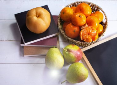 Group of orange fruit put in woven basket,beside blurred Chinese pear,on white timber board,blurry light around