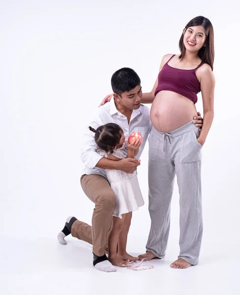 The beautiful pregnant woman standing at the right side,her husband higging little dauther,kneel down and looking at belly,waiting for new born,happy family