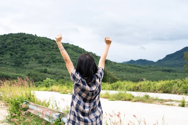 Back side of woman,raising hands up in the air,sing and symbol of charging power from fresh nature,countryside view