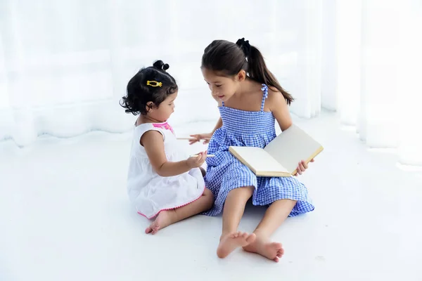 The elder sister holding book and pencil in hand,prepare for teaching younger sister,doing activity together at home, — Stock Image Elder Sister Holding Book Pencil Hand Prepare Teaching Younger Sister Stock Photo