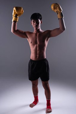 Sarı eldiven giyen ve kırmızı bilek takan yakışıklı adam havaya yumruk atıyor, dik bakıyor, egzersize hazırlanıyor, bulanık ışık yanıyor.