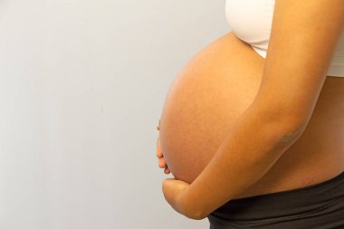 Hamile kadın, karnının genişlediğini gösteriyor. Karın yapısı, gerilmiş deri, arka planın sağ tarafında.