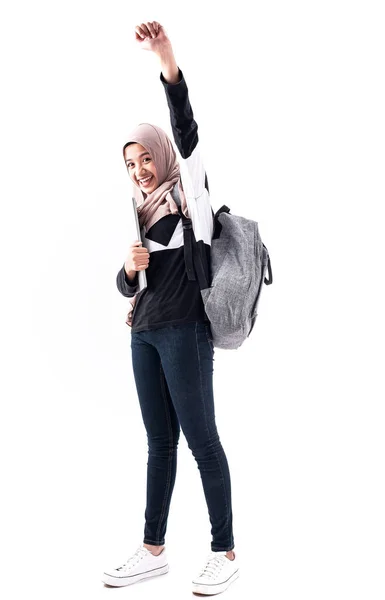 笑顔と幸せな気持ちで 背景に立って 勉強に行く準備をする彼女の腕の中でノートパソコンを抱いて美しいイスラム教徒の女性は 空気中で手を左に上げる — ストック写真