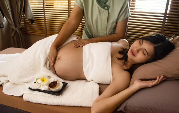 Spa terapisinde tedavi ve rahatlama programı için hamile bir kadının karnına masaj yapan terapist elleri.