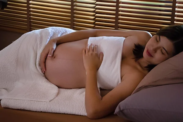 妊娠中の女性はベッドの上に横たわり 白い柔らかい毛布で体を覆い 目を閉じ 彼女の腹を開き マッサージの準備をし 治療し プログラムをリラックス — ストック写真