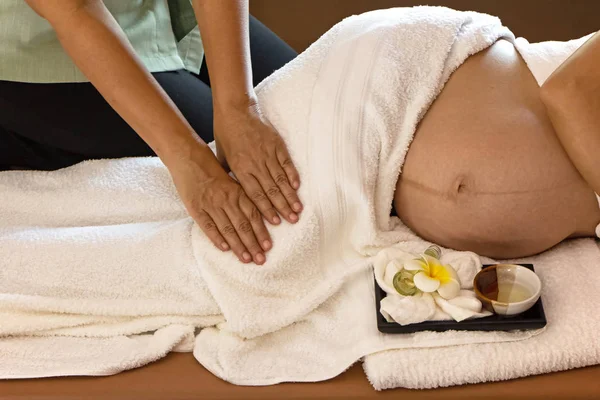 Spa terapisindeki tedavi ve rahatlama programı için hamile bir kadına masaj yapan terapist elleri.