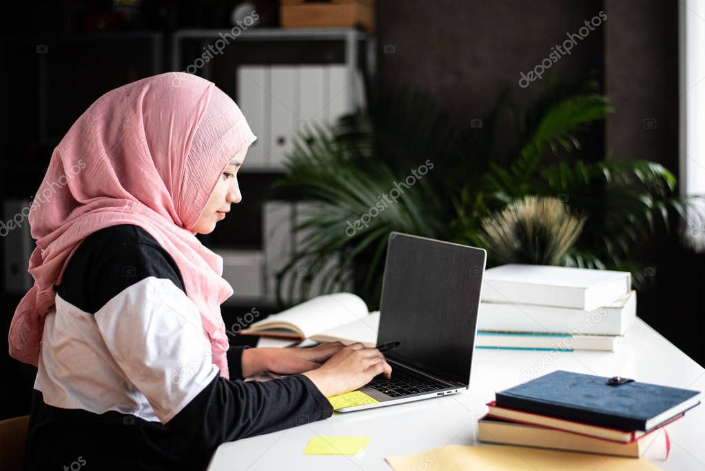 The beautiful muslim woman doing work at home,using laptop for searching data,with interested emotion,blurry light around