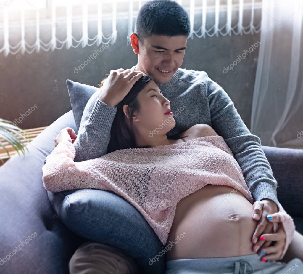 The pregnant woman laying down on sofa and hugging by her husband,put hand touch belly,waith for newborn,with love and care,vintage and art tone,blurry light around