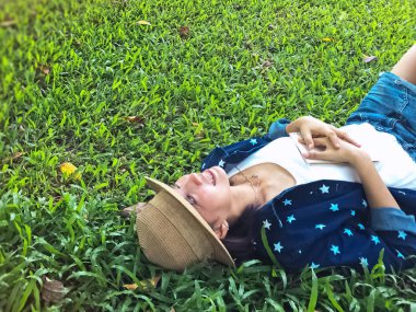 Güzel bayan yeşil çimlere uzanmış, gülümsüyor ve gülümsüyor, bir parkta dinleniyor.