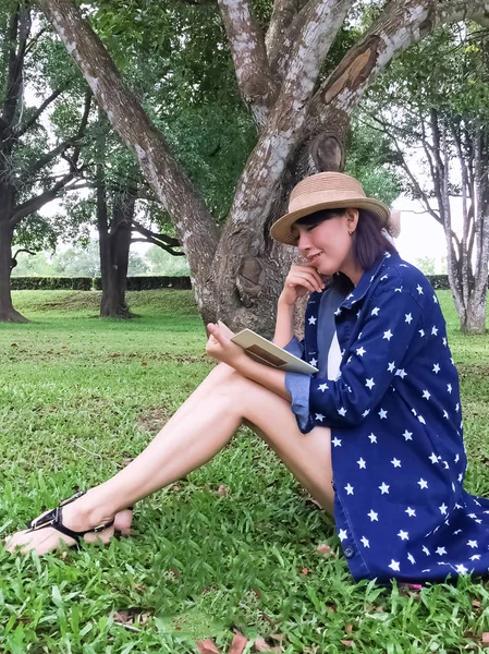 美丽的女人坐在绿草的底层 带着微笑和快乐的心情看书 在公园里度假放松一下 — 图库照片