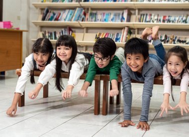 Beş küçük çocuk ahşap masanın yanında oturuyor, kitap okuyor ve konuşuyorlar, birlikte aktiviteler yapıyorlar, okulda mutlu anlar, aydınlatma efekti, bulanık ışık.