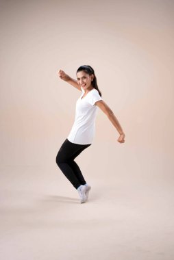 Spor giysili güzel bir bayan, ayakta duran ayaklar diz çöker, adım atar, yumruklarını biraz eğip bükerek egzersiz için dans eder, mutlu bir şekilde.