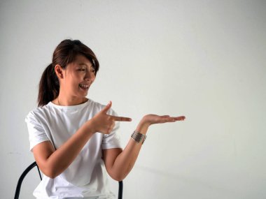 Kadın diş teli takıyor, sandalyeye oturuyor, işaret ediyor ve gülümsüyor. Pozitif duygu.