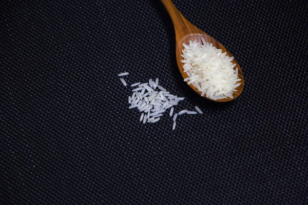 Wood spoon and raw rice on black canvas background